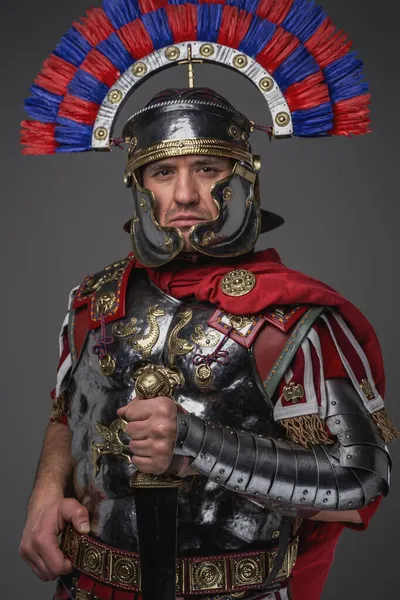Legionário romano com espada posando contra fundo cinza — Fotografia de Stock