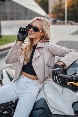 Motosikletiyle şehirde poz veren neşeli bir kadın motorcu.