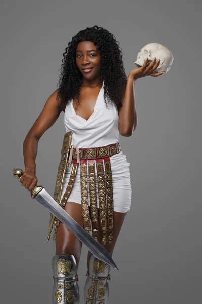 African woman with skull and gladius against gray background — Stock Photo, Image