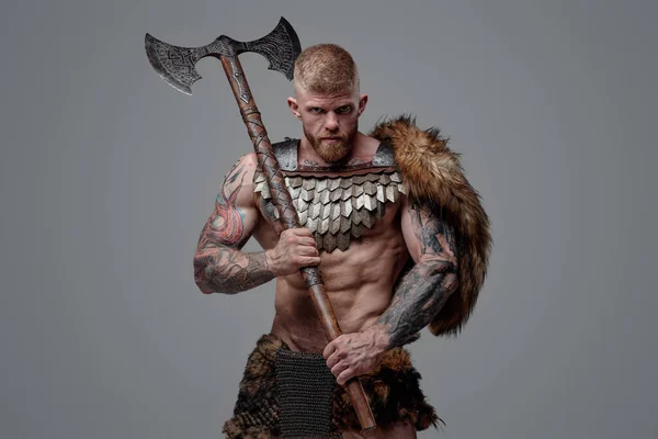 Tattooed muscular viking holding two handed axe on his shoulder