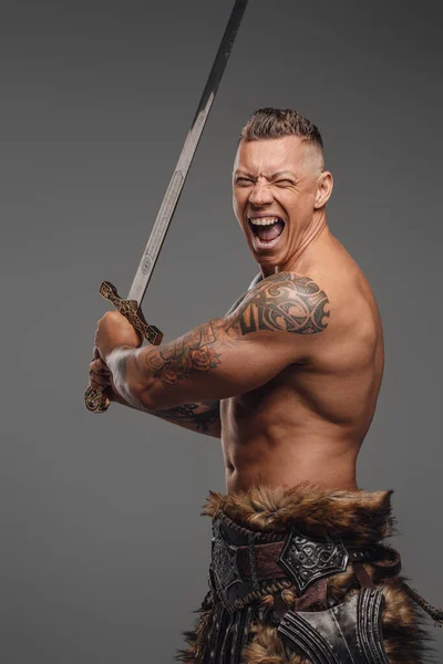 Gewelddadige krijger met tattoos met zwaard tegen grijze achtergrond — Stockfoto