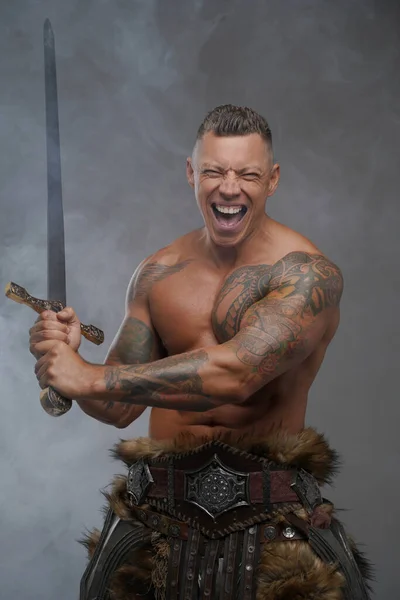 Guerrero tatuado violento con espada aislada sobre fondo gris — Foto de Stock