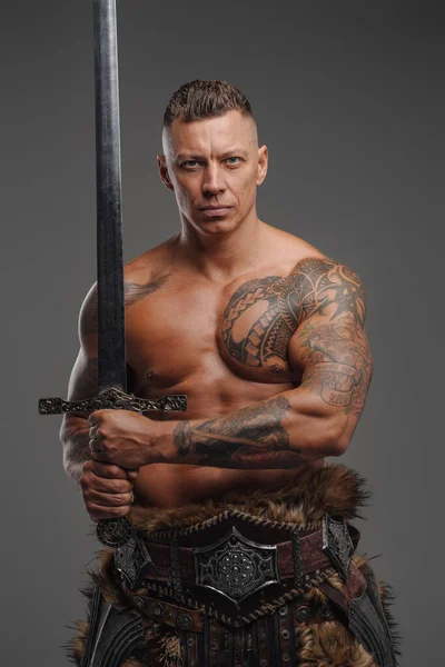 Svalnatý bojovník s nahým trupem drží meč na šedém pozadí — Stock fotografie