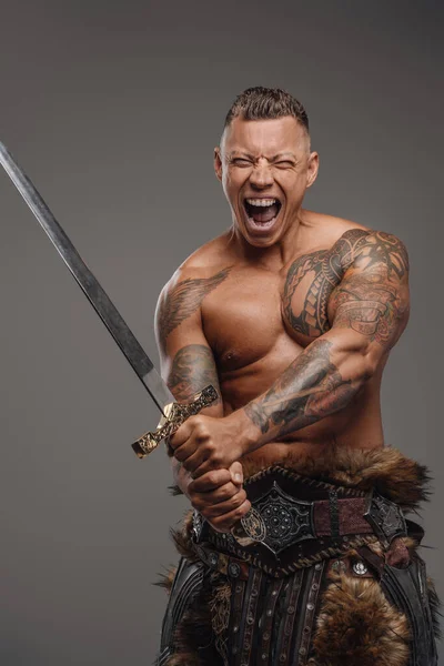 Guerriero violento con tatuaggi che tengono la spada su sfondo grigio — Foto Stock