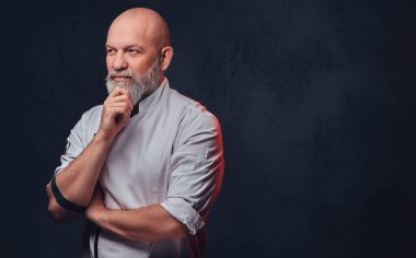 Esmer arka planda üniforma giymiş profesyonel yaşlı bir şef.