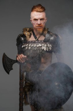 Kızıl saçlı Viking, yara izi, kalkan ve balta taşıyor.