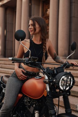 Dövmeli kadın klasik retro motorun üzerinde oturuyor.