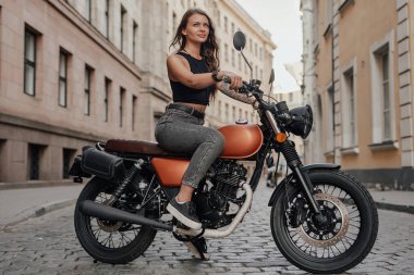 Kahverengi saçlı kadın dışarıda eski moda motosiklet kullanıyor.