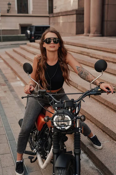 スタイリッシュな女性ポージングオン古典的なダークバイク屋外 — ストック写真