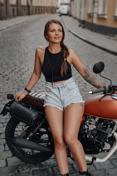 Татуированная мотоциклистка позирует с ретро-велосипедом на открытом воздухе — стоковое фото