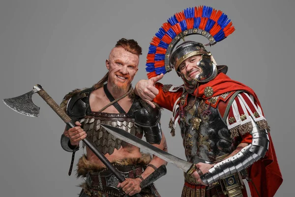 Vreugdevolle viking en Romeinse soldaat poseren tegen grijze achtergrond — Stockfoto