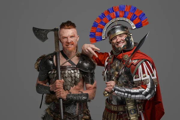 Fröhlicher Wikinger und römischer Soldat posiert vor grauem Hintergrund — Stockfoto