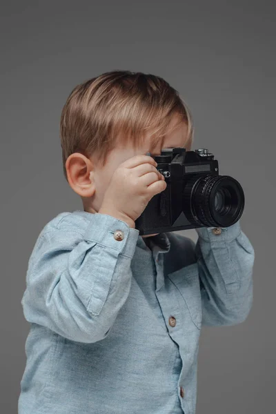 Fotógrafo infantil alegre com câmera contra fundo cinza — Fotografia de Stock