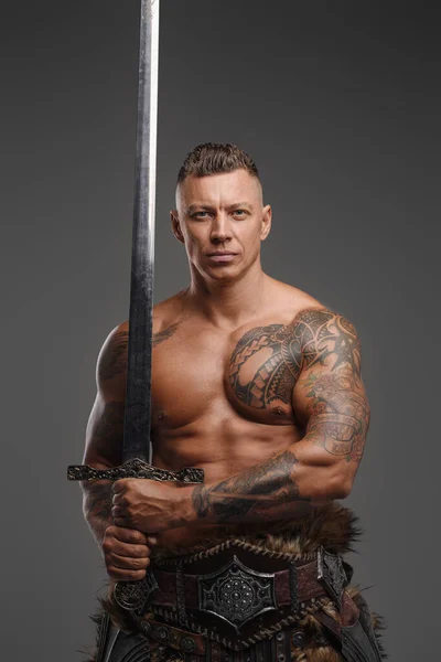 Muskulös krigare med naken bål håller svärd mot grå bakgrund — Stockfoto
