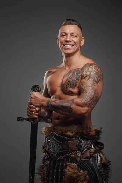 Радостный воин с мускулистым телосложением и мечом, смотрящим в камеру — стоковое фото
