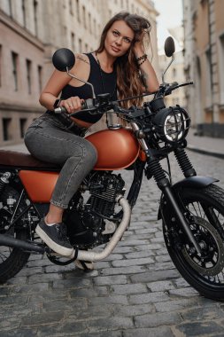 Şehir manzarasına karşı motosiklet üzerinde oturan dövmeli kadın motorcu.