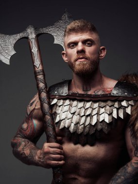 Kameraya baltayla bakan dövmeli Viking portresi.
