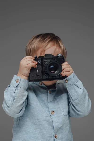 Fröhlicher Kinderfotograf mit Kamera vor grauem Hintergrund — Stockfoto