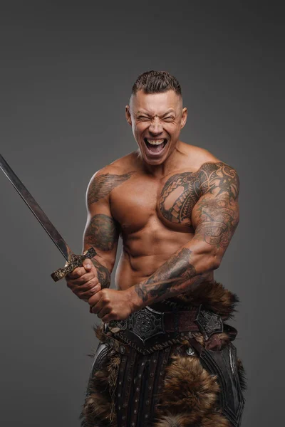 Guerrero violento con tatuajes sosteniendo espada sobre fondo gris — Foto de Stock