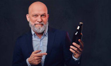 Sakallı ve kel yaşlı adam, elinde şişe, takım elbise giymiş.