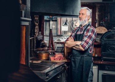 Düşünceli yaşlı şef eski moda et bakkalında poz veriyor.
