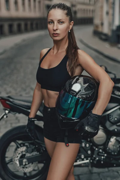 Mulher atraente motociclista e sua bicicleta preta no beco — Fotografia de Stock