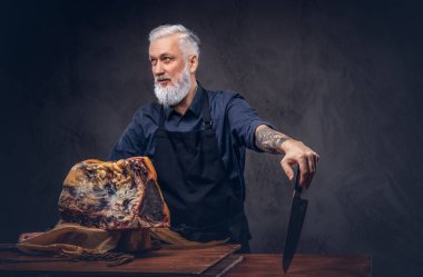 Profesyonel yaşlı kasap masada büyük bir biftek hazırlıyor.