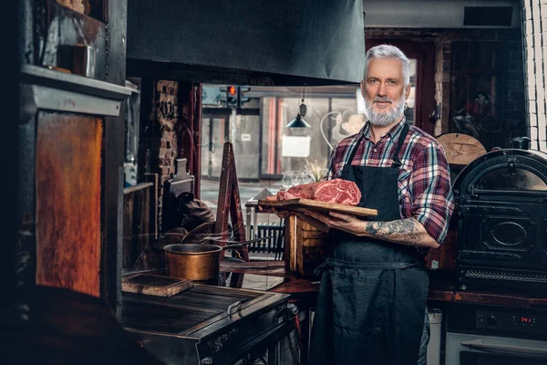 Pewny siebie stary kucharz pozowanie w stylowym sklepie mięsnym — Zdjęcie stockowe