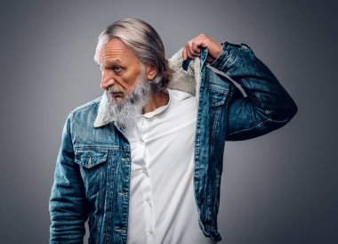 Gri arka planda modern günlük kıyafetler giymiş yaşlı bir adam.