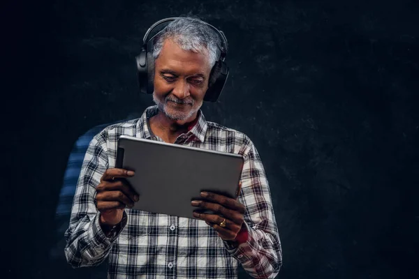 Abuelo con auriculares y tableta contra fondo oscuro — Foto de Stock