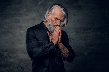 Dua eden yaşlı vücut geliştirici karanlık arka planda kameraya bakıyor.