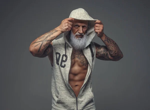Muskularny starzec ubrany w szarą bluzę na szarym tle — Zdjęcie stockowe