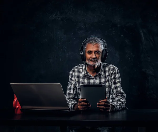 Сучасний старий з ноутбуком сидить за столом на темному тлі — стокове фото