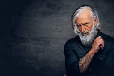 Esmer arka planda poz veren uzun sakallı ciddi bir ihtiyar.