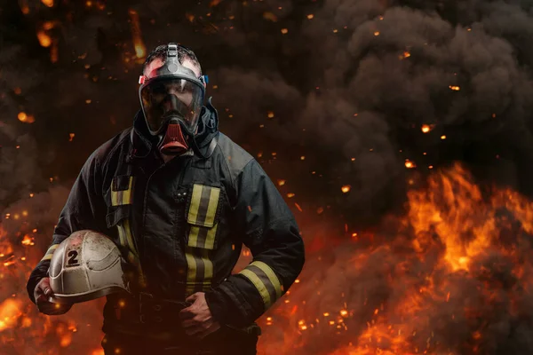 Fireman with gas mask holding hard hat against flame and explosions — Stock Photo, Image
