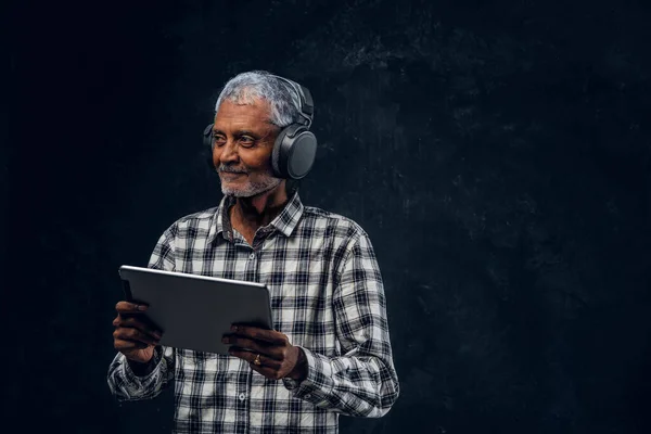 Abuelo con auriculares y tableta contra fondo oscuro — Foto de Stock