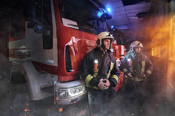 Dos bomberos vestidos con ropa de trabajo con cascos en la estación de bomberos — Foto de Stock