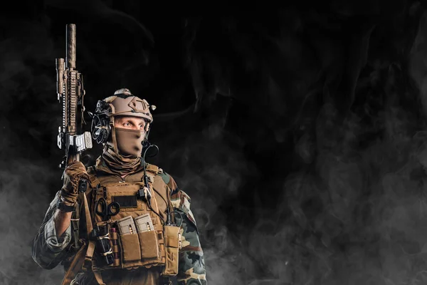 Soldado equipado sosteniendo rifle contra fondo negro con niebla — Foto de Stock