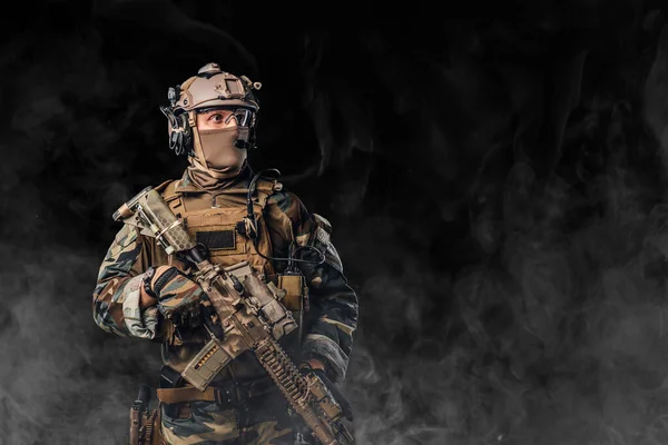 Soldado equipado sosteniendo rifle contra fondo negro con niebla — Foto de Stock