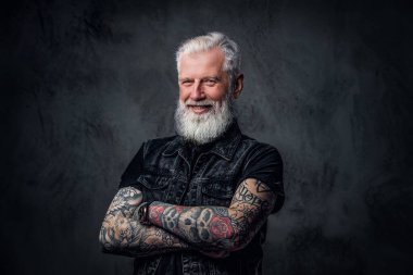 Çapraz kollu, koyu renk giyinmiş neşeli yaşlı bir adam.