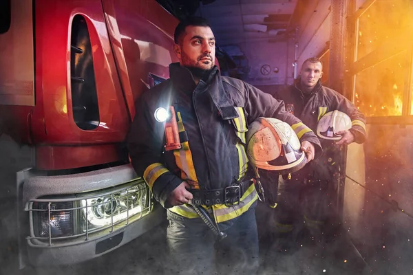 Profesjonalny zespół dwóch strażaków wokół wozu strażackiego w remizie — Zdjęcie stockowe