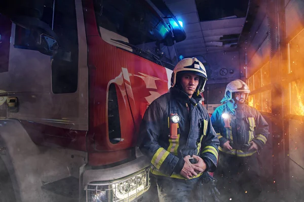 Professionelles Team aus zwei Feuerwehrmännern um Feuerwehrauto im Feuerwehrhaus — Stockfoto