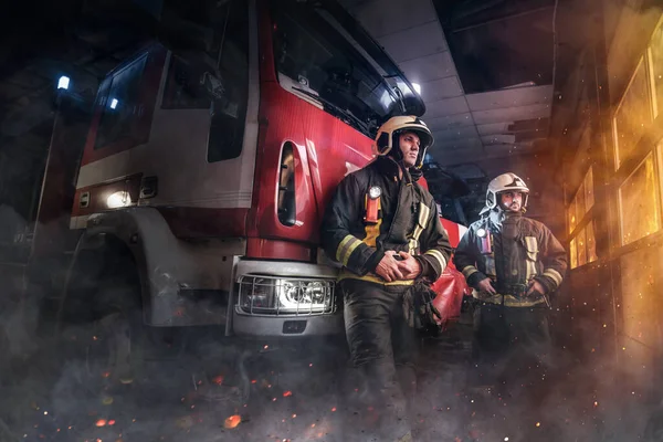 Two firefighters dressed in workwear with helmets in fire station — Stock Photo, Image
