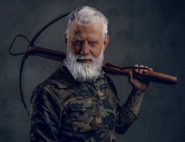 Бородатий старий з сірим волоссям тримає арбалет на плечі — стокове фото