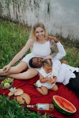 Karışık ırk ailesi nehir kenarında piknik yapıyor.