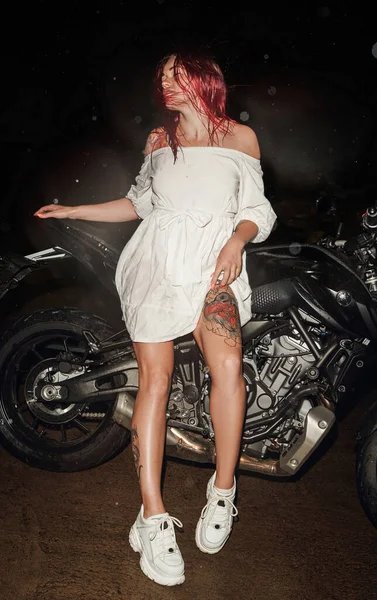 Mulher ruiva com moto preta ao ar livre à noite — Fotografia de Stock