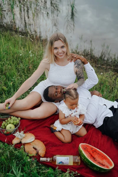 Karışık ırk ailesi nehir kenarında piknik yapıyor.