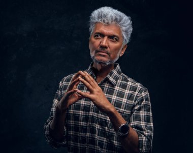 Kareli gömlekli, koyu renk arka planda düşünceli yaşlı bir adam.