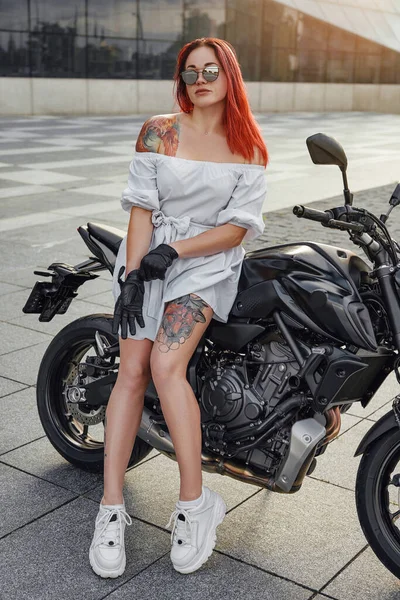 Ruiva mulher motociclista posando na motocicleta preta ao ar livre — Fotografia de Stock
