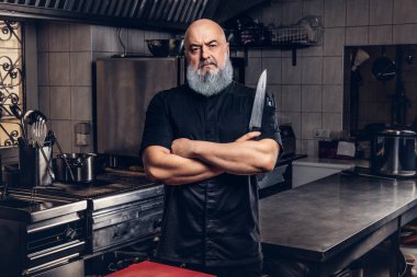 Mutfakta mutfak aletleri tutan gri saçlı şef.